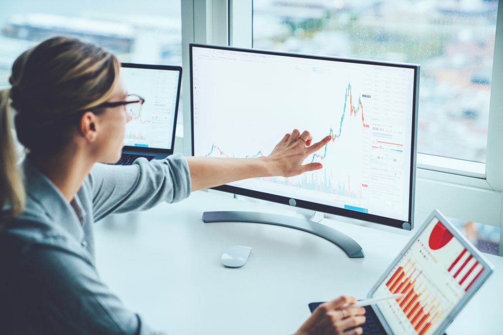 A professional analyzing financial data on dual computer monitors with graphs and charts.