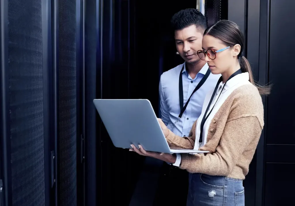 Two people looking at a laptop in a server room.