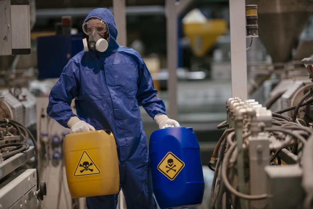 Worker in protective gear handling hazardous materials in an industrial setting.