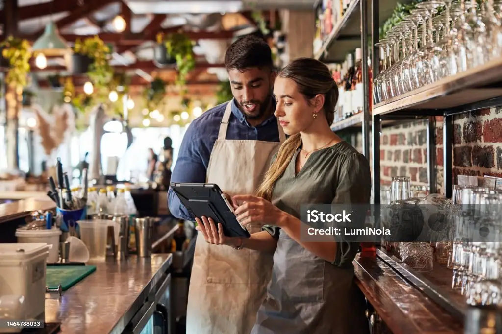 Two baristas in aprons using a digital tablet in a modern cafe.