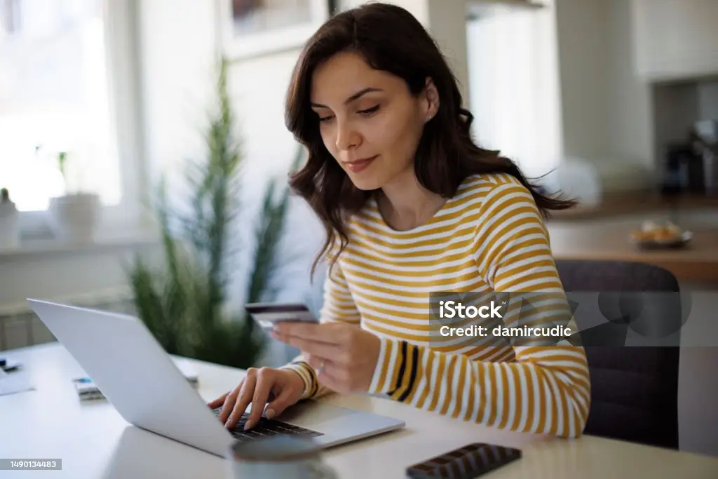 Woman holding a credit card while using a laptop at a home office.